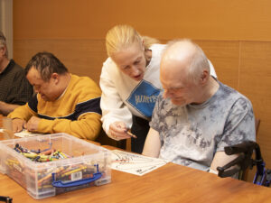 A woman assists a man with disabilities in a craft project.