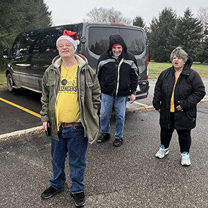three adults in winter coats near a van