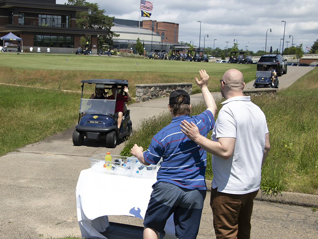 men in a golf cart being greeted by Mam with down syndrome