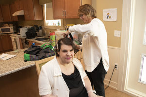 Woman sitting in a kitchen chair getting her hair styled .