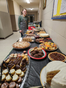 A young women standing by a buffet table of food that is ready to serve.