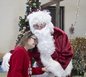A woman with Down syndrome is hugging Santa.