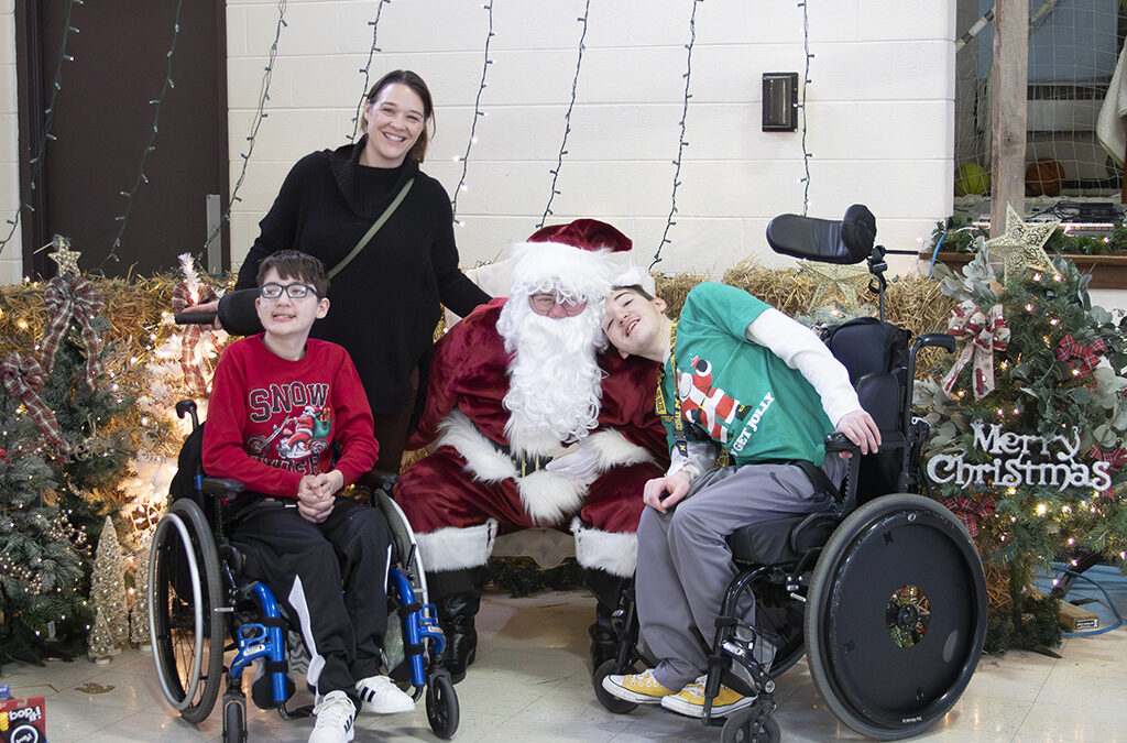 A woman and her two sons in wheelchairs are visiting Santa in the St. Louis Center gym.