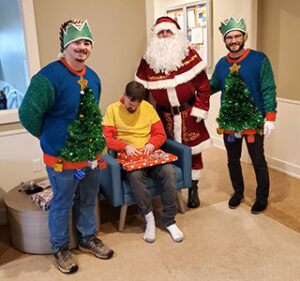 Santa and two elves  with a resident of St. Louis Center in his home.