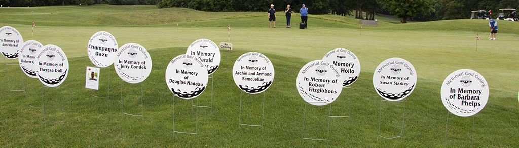 Round golf ball looking signs on a golf course with memorial names on them.