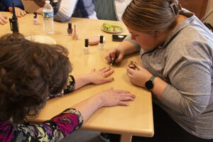 A young woman painting someone's fingernails.